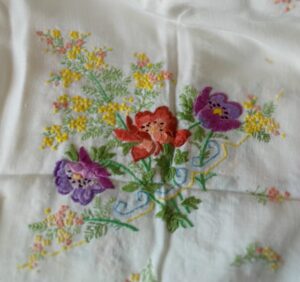 White tablecloth with embroidered flowers, red, purple and yellow.